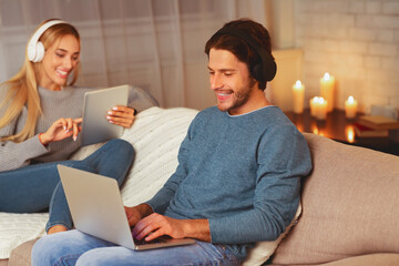 Wall Mural - Boyfriend And Girlfriend Using Gadgets Digital Tablet And Laptop Relaxing On Sofa Spending Weekend At Home. Selective Focus