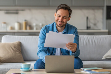Poster - A man is sitting on a sofa, smiling as he reviews some documents while using a laptop computer. He is wearing a blue denim shirt, and the sofa is in a home living room.