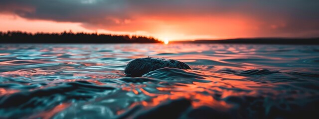 Wall Mural -  A sunset over a tranquil body of water, featuring a solitary rock in its center, and trees silhouetted against the backdrop