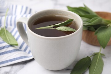 Poster - Aromatic herbal tea in cup with sage on white table, closeup