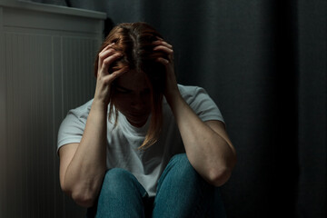 The woman in the photo looks depressed and scared, she has suffered from domestic violence or emotional abuse. Her posture is hunched, and her facial expression is anxious and sad