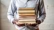 © Sniezka - Dark-skinned Man holding stack of books, business casual attire, plaid shirt, white background, neutral tones, ideal for educational websites and professional presentations.