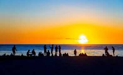 Wall Mural - People on the beach of Flic en Flac in Mauritius at a colorful sunset. Silhouettes of holidaymakers and locals enjoying the play of lights over the horizon. Tourist destination on the tropical island.