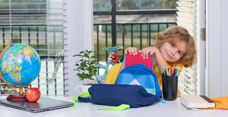 Fototapete - Portrait of nerd student puts school supplies and books in a backpack. Preparation for school. Pupil kid preparing school homework, sitting at table.