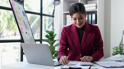 Wall Mural - Asian businesswoman working on laptop and calculating with financial calculator from graphs, statistics, charts, planning, real estate, business success results in modern office.