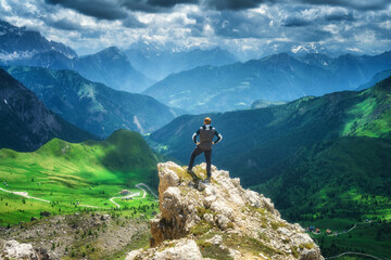 Wall Mural - man on the rock in alpine mountains, green meadows at sunset