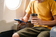 © NanSan - A man travels abroad by plane, sitting near the window. He holds a coffee mug, looks at his phone, and uses an airline credit card while interacting with messengers during the flight.
