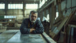 © VK Studio - A pensive man leans on a workbench in an industrial workshop, bathed in natural light from large windows, reflecting contemplation.