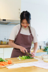 Asian women chopping slices lettuce with knife on cutting board to preparing fresh vegetables of ingredients for cooking breakfast meal while making healthy food lifestyle in the kitchen at home