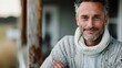 ©  lukaPixMedia - A grey-haired man with a gentle smile and crossed arms stands in his knit sweater, radiating warmth and comfort in an outdoor setting, exemplifying peaceful and content living.