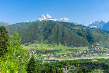 Wall Mural - Mountains covered with forest and bushes. Villages in the valley. Snow capped peak of Mount Ushba