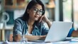 © Lakkhana - Businesswoman reviewing financial projections on a laptop, looking determined