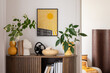 © FollowTheFlow - Stylish interior with a wooden cabinet plants, decorative objects, and books. A vibrant mock up art piece featuring a sunburst design adds a pop of color. Minimalist home decor. Template.