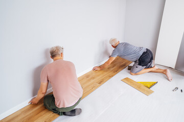 Wall Mural - Father and adult son installing flooring in new Home by their own. Doing measurements, calculating for vinyl laminate and skirting. DIY, Do it yourself. Home renovation, improvement, refurbishment.