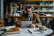 © Milos - A man in a brown suit is focused on using a tablet while sitting at a marble-top table in a stylish café, with shelves filled with items in the background.