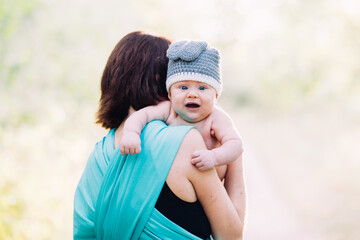 Young mother holding her baby boy in hands, outdoors in summer in sun rays