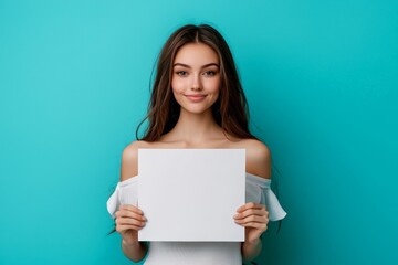 a beautiful young girl holding up a blank piece of paper - studio portrait on blue background - mockup template