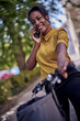© kerkezz - Happy young woman with bicycle using mobile phone in city park, smiling.