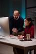 © Mediaphotos - Vertical portrait of cybersecurity team of two people using computer together in office lit by blue light