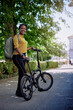 © kerkezz - Portrait of a young smiling woman standing next to a bicycle with a backpack.