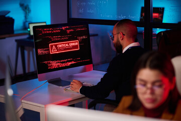 Cybersecurity department office with critical error message on computer screen in red neon lights copy space