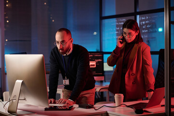 Portrait of two people working in cybersecurity department with red neon light critical emergency situation