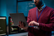 © Mediaphotos - Close up of bearded adult man holding laptop standing in IT development office with blue lights copy space