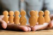 © Worrapol - Protecting Our People: A pair of hands cradles a circle of wooden figurines, symbolizing the importance of caring for and protecting employees in the workplace.  The warm, natural tones of the wood an