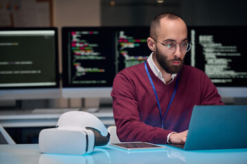 Portrait of bearded adult man wearing glasses and using laptop at desk in IT development office , copy space