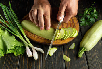 Wall Mural - Cooking lecho from vegetables on the kitchen table. Cutting zucchini with a knife in the hands of the cook. Vegetable menu for dinner.