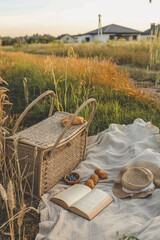 Wall Mural - Picnic setup with a woven basket, book, straw hats, croissants, and blueberries on a blanket. Set against a golden wheat field backdrop, capturing a serene countryside atmosphere