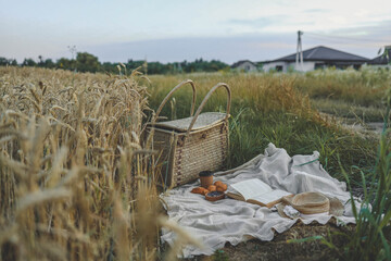 Wall Mural - Picnic setup with a woven basket, book, straw hats, croissants, and blueberries on a blanket. Set against a golden wheat field backdrop, capturing a serene countryside atmosphere