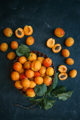 Wall Mural - Fresh apricots in a wooden bowl and scattered on a dark surface. Some apricots are halved, revealing their pits, highlighting the vibrant colors and natural textures of the fruit