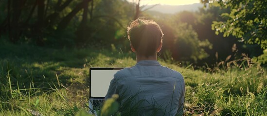 A young man works on a laptop outdoors amid nature creating an alternative office space The laptop displays a blank screen inviting custom text or design in the copy space image