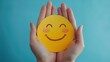 © Supakrit - Closeup of hands holding a yellow smiley face on a blue background.