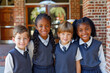 © Running opossum - Four cheerful elementary school students in uniform standing together outside school building