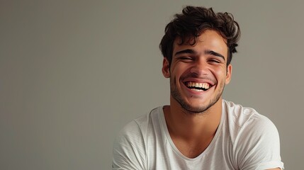 Capture a young Brazilian man in casual fashion, posed against a neutral gray background, laughing with a relaxed expression