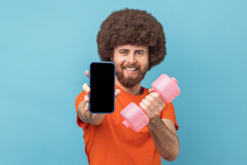 Wall Mural - portrait of happy man with afro hairstyle wearing orange t-shirt holding dumbbell and mobile phone w