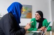 © Studio Marmellata - Two women in hijabs having a productive discussion in a modern office, using laptops and sharing ideas to achieve their project goals.