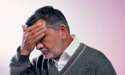 Wall Mural - Medium shot portrait video of a man in his 50s pressing his temple due to a migraine wearing a chic cardigan against a pastel or soft colors background 