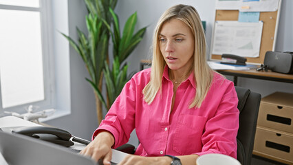 Sticker - Focused young blonde woman working diligently at her desk in a bright modern office setting.