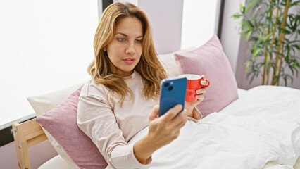 Poster - Hispanic woman sitting in her bedroom drinking coffee and using smartphone