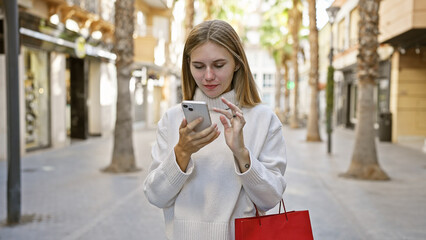 Sticker - A young caucasian woman with blonde hair and blue eyes using a smartphone on a sunny urban street while shopping.