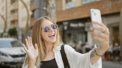 Sticker - A cheerful blonde woman in sunglasses taking a selfie on a busy city street.