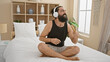 © Krakenimages.com - A smiling bearded man wearing headphones combs his hair while sitting on a bed in a sunlit bedroom