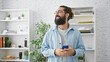 © Krakenimages.com - A smiling hispanic man with a beard stands in a modern office, holding a phone and wearing glasses.