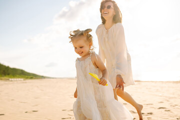 Mommy walks with her daughter on beach during holiday vacation at sunset. Travel, tourism, weekend concept. Family party.