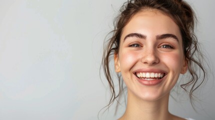 a cheerful young woman with a bright smile and clear white teeth expresses joy, set against a simple