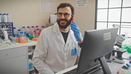 A middle-aged man with a beard smiling while talking on a mobile phone in a laboratory.