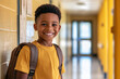 © AISTEL - cheerful little black boy student with backpack walking through the elementary school hallway, confidently smiling at the camera. Back to school concept. copy space for text.
